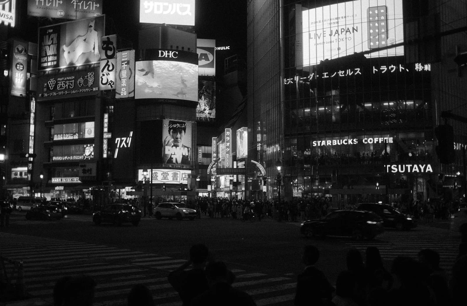 Black and white night scene of pedestrians crossing Shibuya Crossing in Tokyo